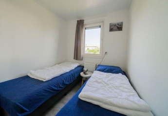 Habitación con dos camas individuales, ropa de cama azul, ventana y mesa pequeña en el Pavilion de EuroParcs Veluwemeer.