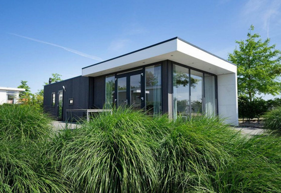 Moderne Pavilion Waterfront lodge met grote glaspartijen en tuinen, gefotografeerd bij blauwe lucht.