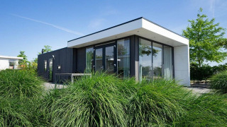 Moderne Pavilion Waterfront-lodge med store vinduer og haver, fotograferet under en klar blå himmel.