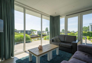 Stue i Pavilion Waterfront-lodge på EuroParcs Veluwemeer, Holland, med udsigt over vand og natur.