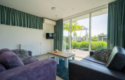 Sala en la lodge Pavilion Waterfront de EuroParcs Veluwemeer con amplios ventanales y vista al jardín exterior.