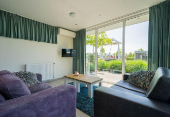 Sala en la lodge Pavilion Waterfront de EuroParcs Veluwemeer con amplios ventanales y vista al jardín exterior.