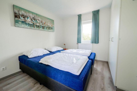 Chambre lumineuse avec deux lits simples, couvertures bleues, armoire et fenêtre au Pavilion Waterfront, EuroParcs Veluwemeer.