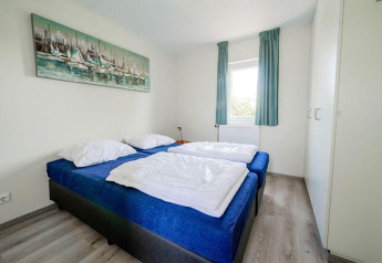 Dormitorio luminoso con dos camas individuales, cubrecamas azules, armario y ventana en Pavilion Waterfront, EuroParcs Veluwemeer.