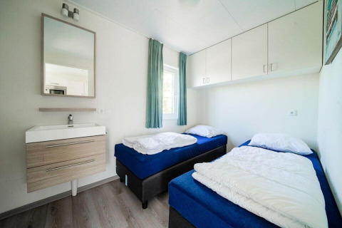 Chambre lumineuse et moderne avec deux lits simples, fenêtre, lavabo et miroir au Pavilion Waterfront, EuroParcs Veluwemeer.