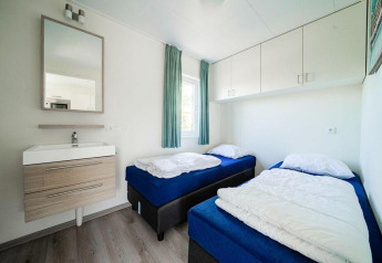 Chambre lumineuse et moderne avec deux lits simples, fenêtre, lavabo et miroir au Pavilion Waterfront, EuroParcs Veluwemeer.