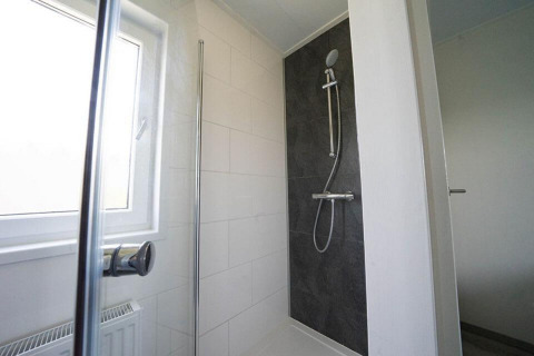 Douche moderne au Pavilion Waterfront lodge à EuroParcs Veluwemeer, Pays-Bas, avec grande fenêtre et carrelage noir.
