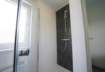 Moderne douche in Pavilion Waterfront lodge bij EuroParcs Veluwemeer, Nederland, met groot raam en donkere tegels.