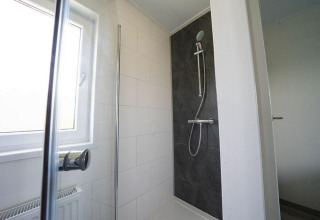 Douche moderne au Pavilion Waterfront lodge à EuroParcs Veluwemeer, Pays-Bas, avec grande fenêtre et carrelage noir.