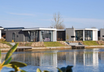 Moderne pavillonhytter ved vandet på EuroParcs Veluwemeer, Holland, omgivet af natur og blå himmel.