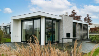 Moderne Pavilion Waterfront lodge met grote ramen, omgeven door gras en een stralend blauwe lucht.
