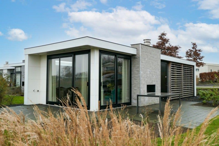 Modern Pavilion Waterfront lodge with large glass windows, surrounded by grass and a bright blue sky.