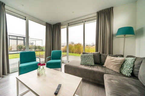 Salon lumineux au lodge Pavilion Waterfront d’EuroParcs Veluwemeer aux Pays-Bas, avec mobilier moderne et grandes fenêtres.
