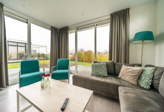 Salon lumineux au lodge Pavilion Waterfront d’EuroParcs Veluwemeer aux Pays-Bas, avec mobilier moderne et grandes fenêtres.