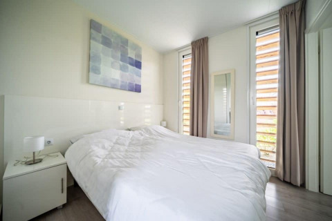 Chambre moderne et lumineuse au Pavilion Waterfront, EuroParcs Veluwemeer, avec grand lit et hautes fenêtres.