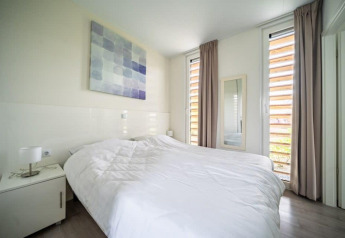 Dormitorio moderno y luminoso en Pavilion Waterfront, EuroParcs Veluwemeer, con cama grande y ventanas altas.