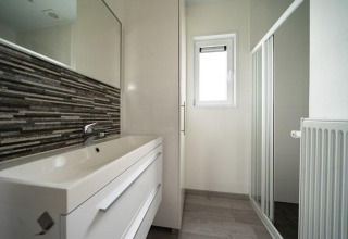 Baño moderno en Pavilion Waterfront, EuroParcs Veluwemeer, con ducha acristalada, ventana y lavabo.