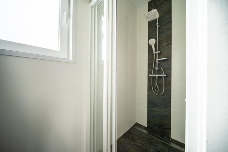 Ducha moderna con puerta de cristal y muro de azulejos oscuros en Pavilion Waterfront, EuroParcs Veluwemeer.