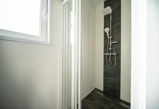 Ducha moderna con puerta de cristal y muro de azulejos oscuros en Pavilion Waterfront, EuroParcs Veluwemeer.