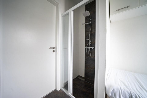 Baño minimalista con ducha, puerta blanca y cama en Pavilion Waterfront, EuroParcs Veluwemeer, Países Bajos.