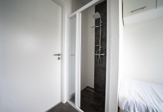 Baño minimalista con ducha, puerta blanca y cama en Pavilion Waterfront, EuroParcs Veluwemeer, Países Bajos.