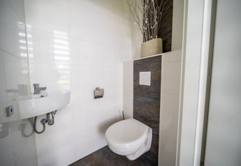 Moderne, minimalistisk badeværelse med væghængt toilet, lille håndvask og dekorativ vase på hylden.