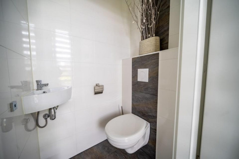 Bagno moderno minimalista con wc sospeso, piccolo lavandino e vaso decorativo su mensola superiore.