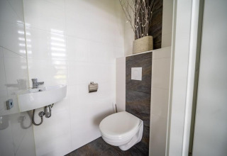 Salle de bain moderne minimaliste avec WC suspendu, petit lavabo et vase décoratif sur l’étagère du fond.