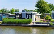 Moderne pavillon ved vandkanten i EuroParcs Veluwemeer, Holland, omgivet af grønne planter og vand.