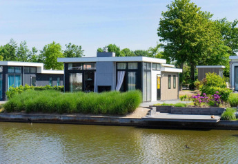 Moderne pavillon ved vandkanten i EuroParcs Veluwemeer, Holland, omgivet af grønne planter og vand.