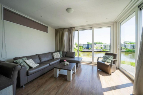 Lyst opholdsområde med hjørnesofa, lænestol, store vinduer og udsigt over vandet på Pavilion Waterfront.