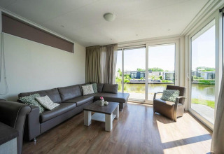 Helles Wohnzimmer mit Ecksofa, Sessel und großen Fenstern mit Blick auf das Wasser im Pavilion Waterfront.