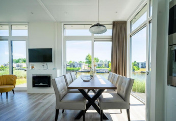 Lichte eetruimte in Pavilion Waterfront-lodge bij EuroParcs Veluwemeer met grote ramen en zicht op het meer.