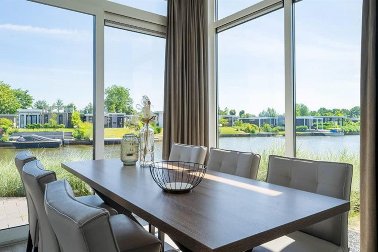 Essbereich mit großen Fenstern und Blick auf das Wasser und moderne Lodges im Pavilion Waterfront bei EuroParcs Veluwemeer.
