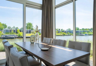Spisestue med store vinduer og udsigt til vandet og moderne hytter i Pavilion Waterfront ved EuroParcs Veluwemeer.