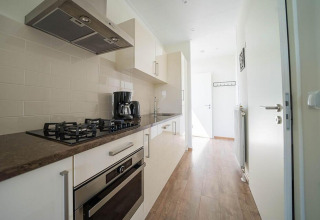 Cocina moderna y estrecha en Pavilion Waterfront de EuroParcs Veluwemeer, Países Bajos, con estufa y cafetera.