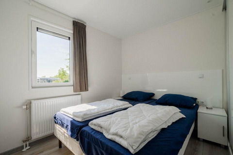 Dormitorio luminoso con dos camas individuales, ropa de cama azul y ventana en Pavilion Waterfront, EuroParcs Veluwemeer.