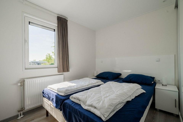 Helles Schlafzimmer mit zwei Einzelbetten, blauer Bettwäsche und Fenster im Pavilion Waterfront, EuroParcs Veluwemeer.