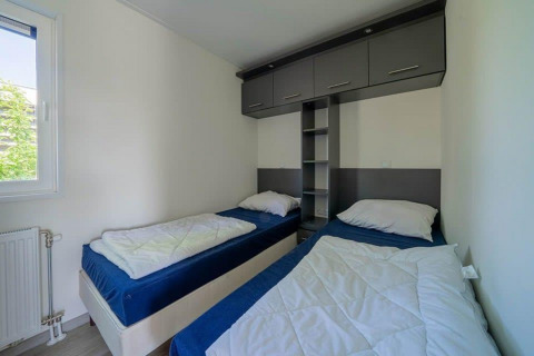 Habitación con dos camas individuales, cubrecamas azules, paredes blancas y armarios en Pavilion Waterfront, EuroParcs Veluwemeer.