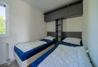 Habitación con dos camas individuales, cubrecamas azules, paredes blancas y armarios en Pavilion Waterfront, EuroParcs Veluwemeer.