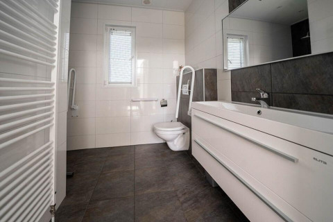 Moderne badkamer met wandtoilet, wastafel en grote tegels in de Pavilion Waterfront lodge.