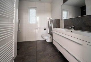 Moderne badkamer met wandtoilet, wastafel en grote tegels in de Pavilion Waterfront lodge.