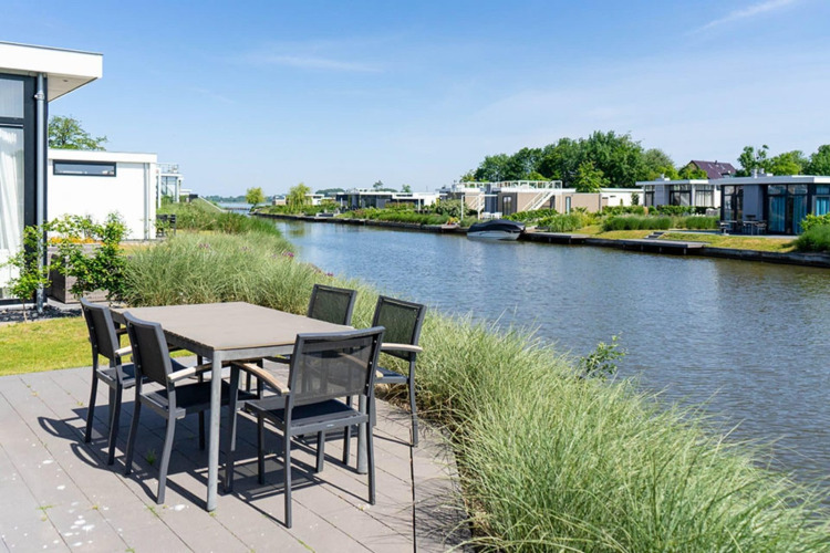 Terrasse mit Esstisch an der Pavilion Waterfront-Lodge mit Kanalblick bei EuroParcs Veluwemeer, Niederlande.