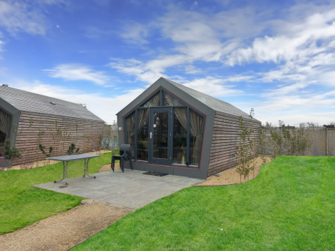 Udsigt til Solo Retreat lodge med træbeklædning, terrasse, græsplæne og klar blå himmel.