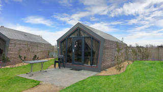 Udsigt til Solo Retreat lodge med træbeklædning, terrasse, græsplæne og klar blå himmel.