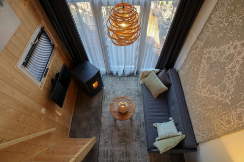 Acogedora sala de estar en una Tiny House de EuroParcs Veluwemeer con sofá, estufa y grandes ventanales.