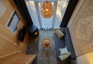 Acogedora sala de estar en una Tiny House de EuroParcs Veluwemeer con sofá, estufa y grandes ventanales.