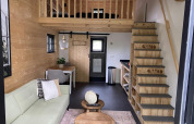 Interior elegante de una tiny house en EuroParcs Veluwemeer, Países Bajos, con altillo, sofá y paredes de madera.