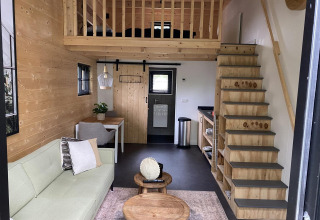 Interior elegante de una tiny house en EuroParcs Veluwemeer, Países Bajos, con altillo, sofá y paredes de madera.