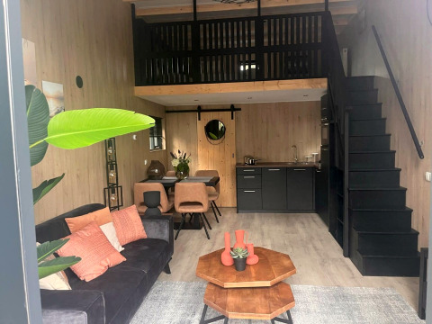 Modernes Glamping-Unterkunft mit Wohnzimmer, Küche, Essbereich und Hochbett in warmen Holztönen.